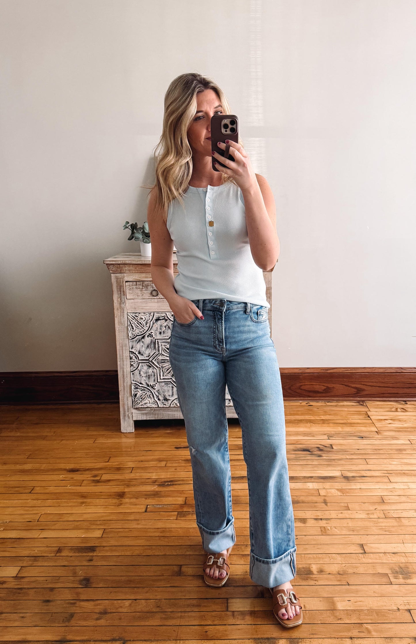 Woman taking a mirror selfie wearing a white top and blue jeans in a room with wooden flooring.