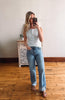 Woman taking a mirror selfie wearing a white top and blue jeans in a room with wooden flooring.
