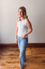Woman wearing a light blue sleeveless top and jeans standing on a wooden floor.