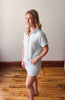 Woman wearing a light blue button-up dress standing on a wooden floor.