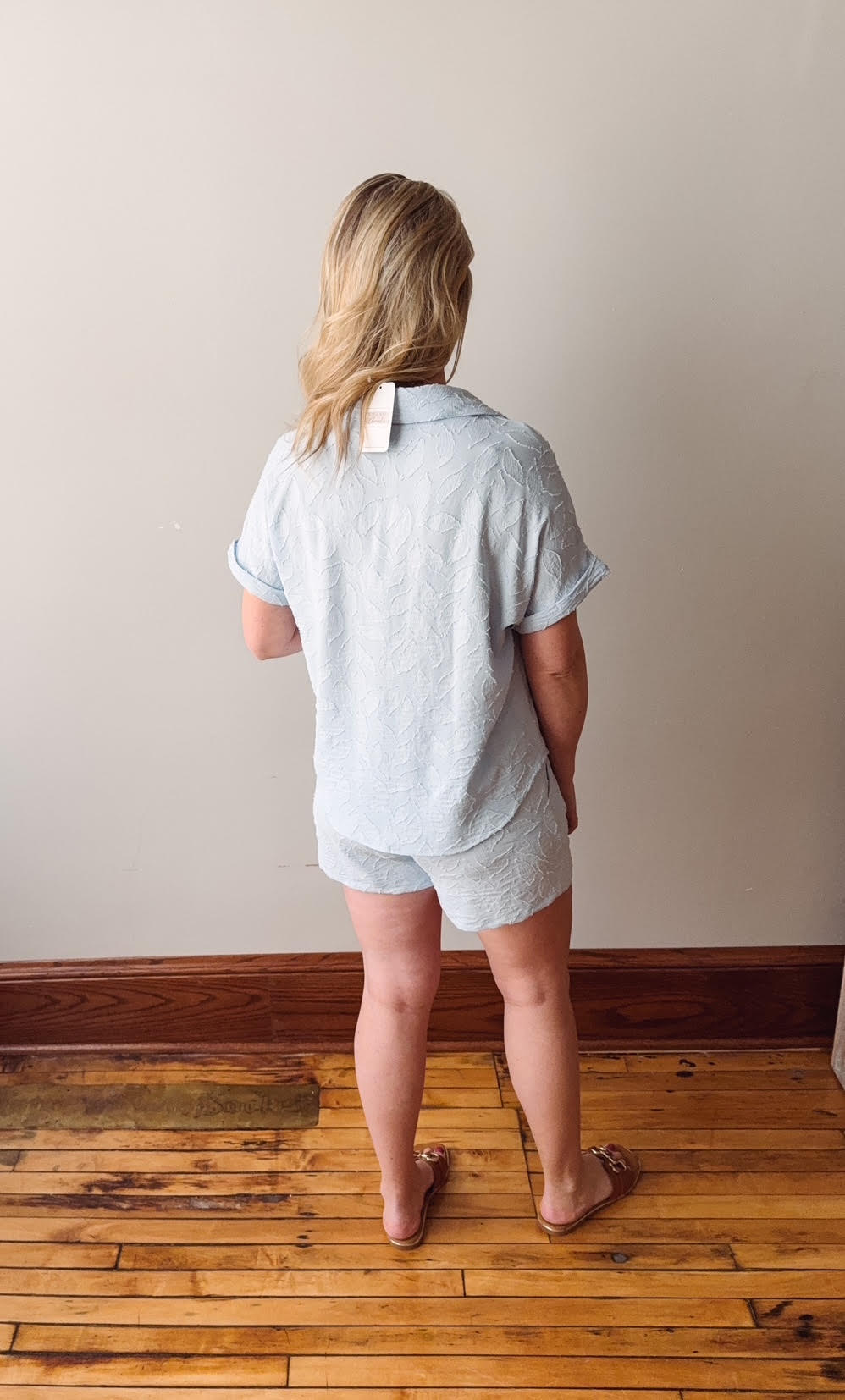 Person wearing a light gray outfit standing on a wooden floor with a plain wall background
