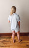 Person wearing a light gray outfit standing on a wooden floor with a plain wall background