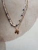 Two pearl necklaces with blue accents and a gold bow pendant on a textured surface.