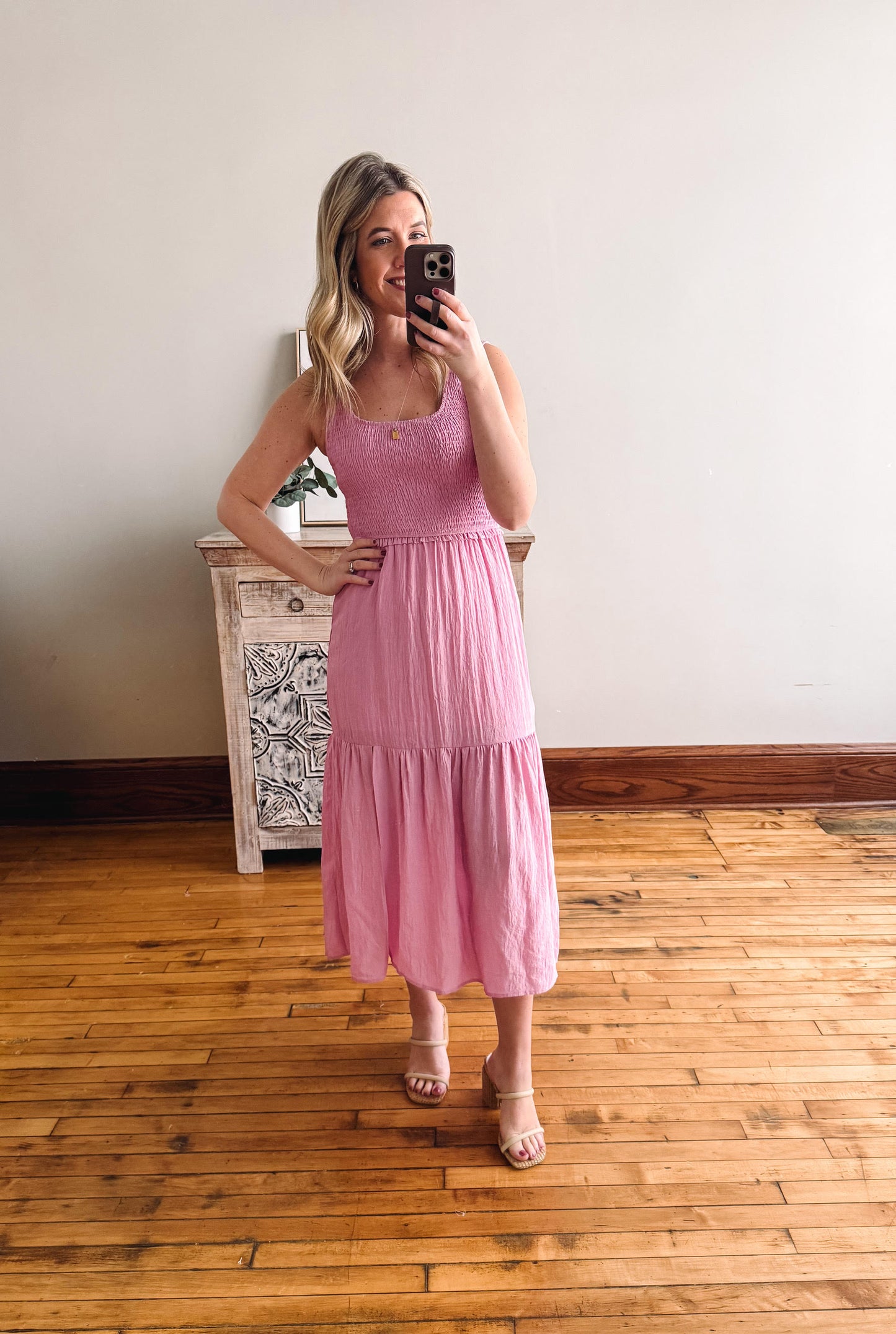 Woman taking a mirror selfie wearing a pink dress in a room with wooden flooring.