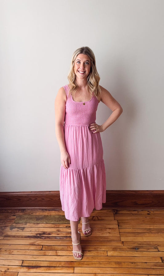 Woman wearing a pink dress standing on a wooden floor against a white wall