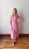 Woman wearing a pink dress standing on a wooden floor against a white wall