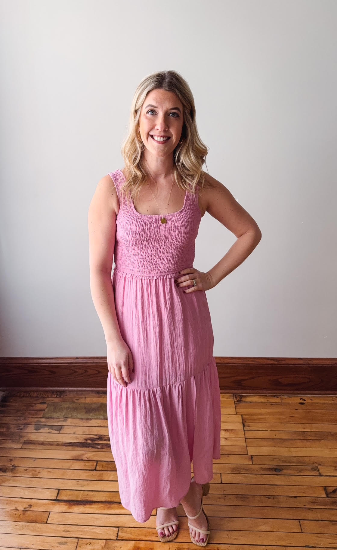 Woman wearing a pink dress standing on a wooden floor with a white wall background