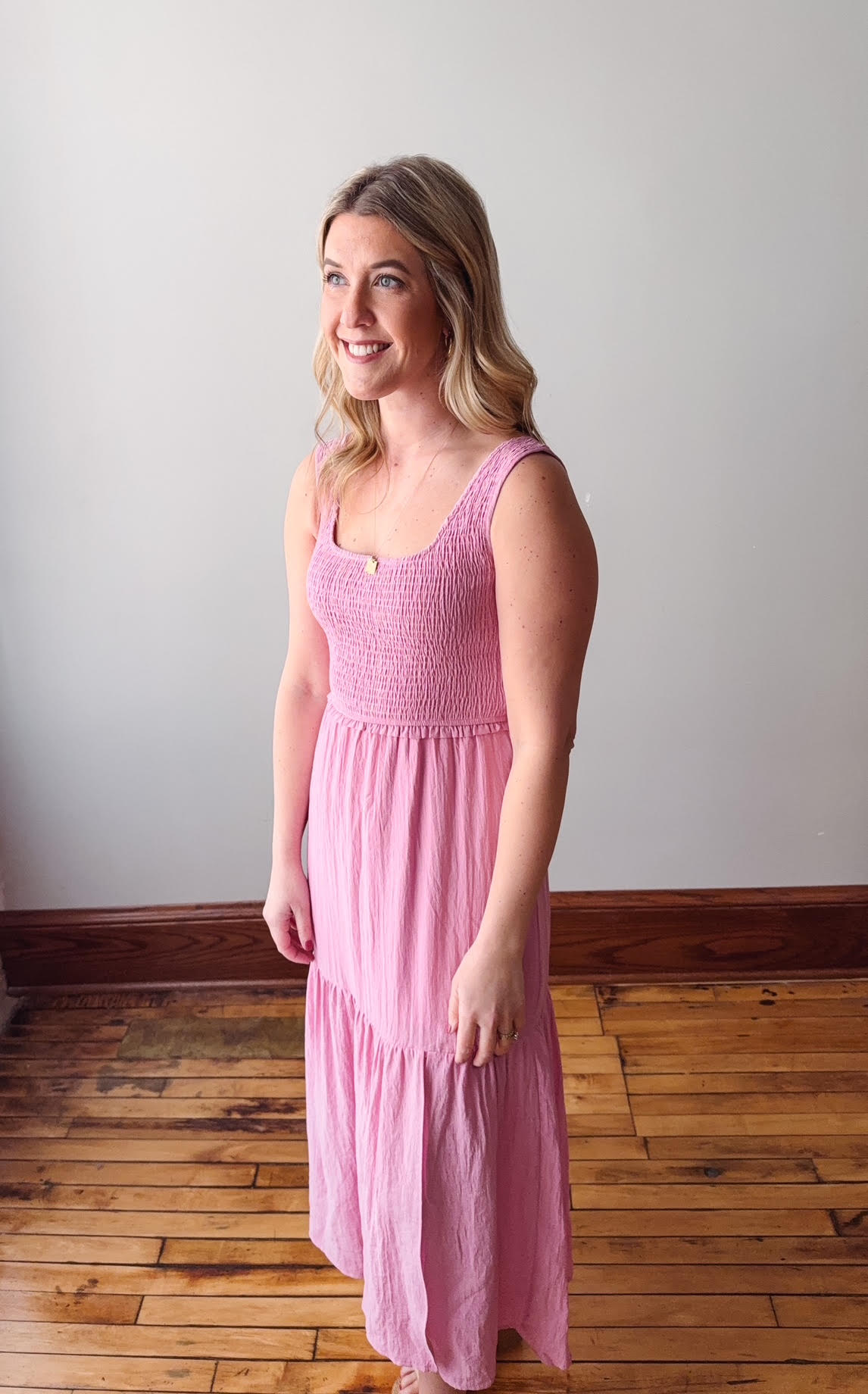 Woman wearing a pink dress standing on a wooden floor with a white wall background