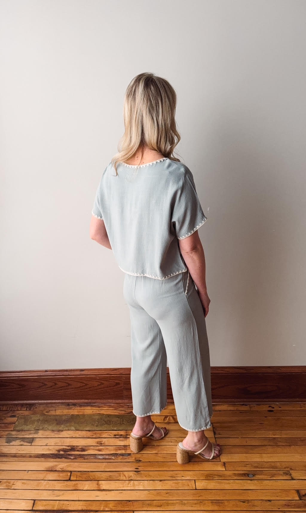 Woman wearing a light blue outfit standing on a wooden floor with a plain wall background