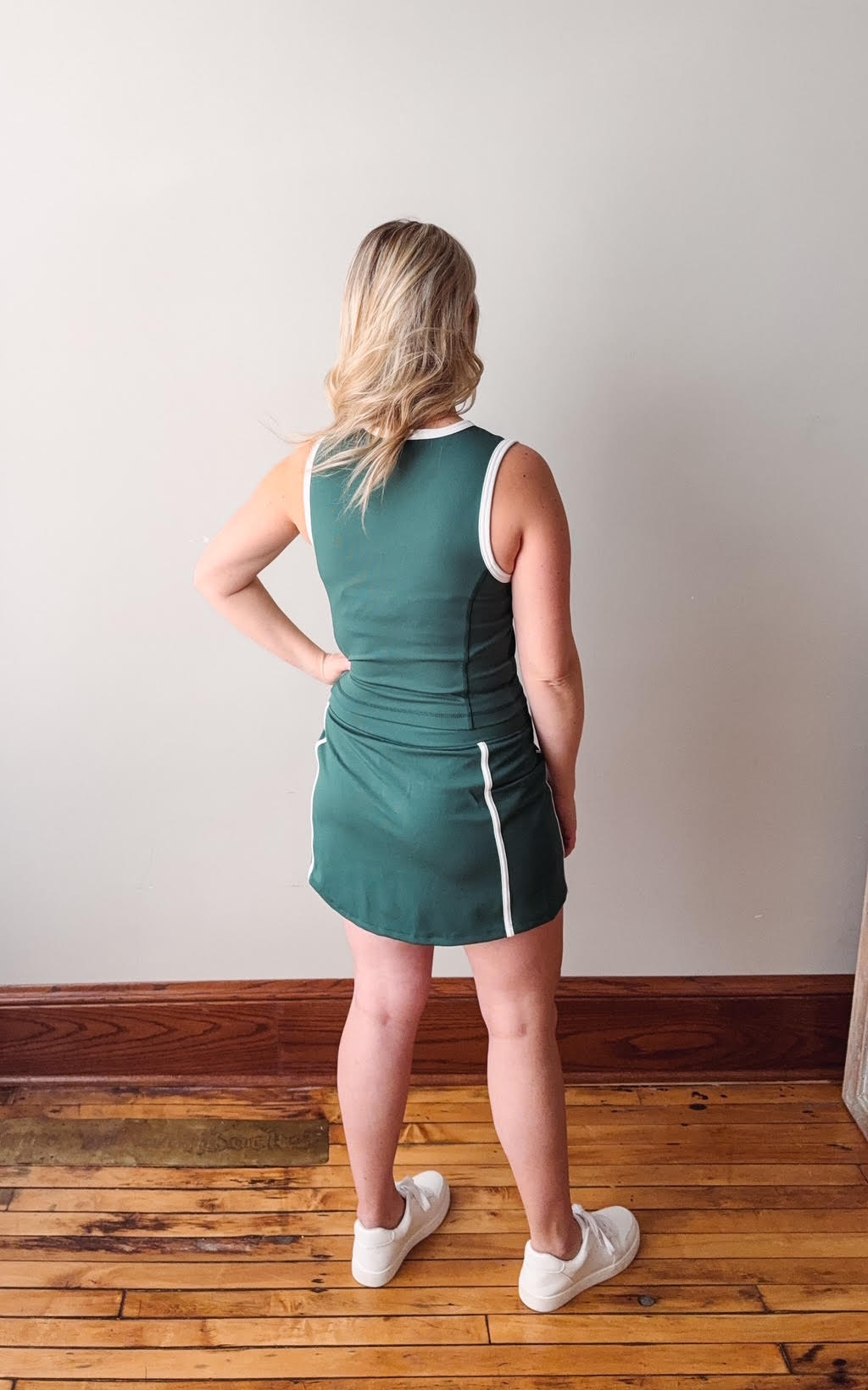 Woman wearing a green dress standing on a wooden floor with a white wall background
