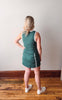 Woman wearing a green dress standing on a wooden floor with a white wall background
