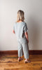 Woman wearing a light blue outfit standing on a wooden floor with a plain wall background