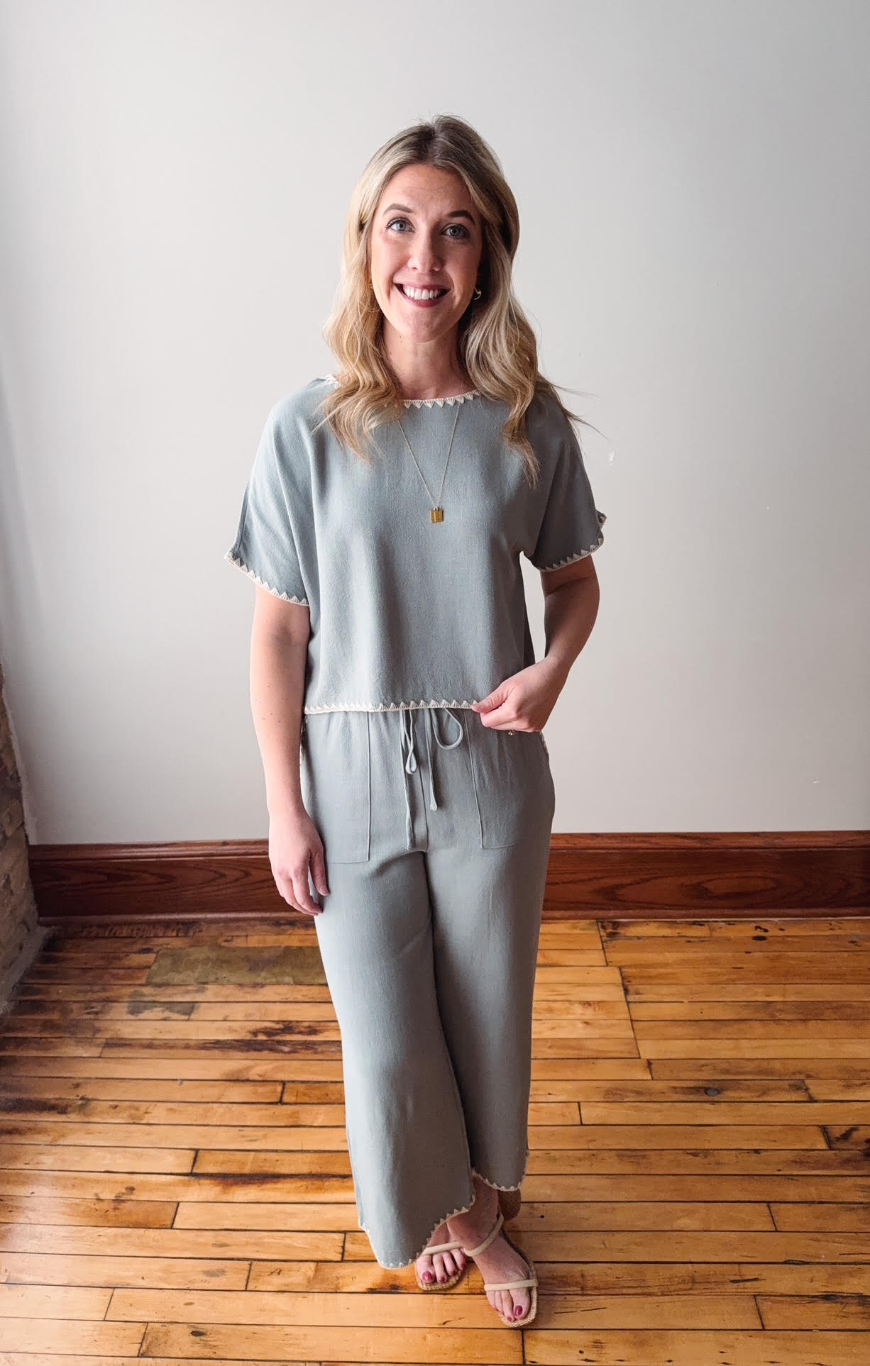 Woman wearing a light gray outfit standing on a wooden floor with a white wall background