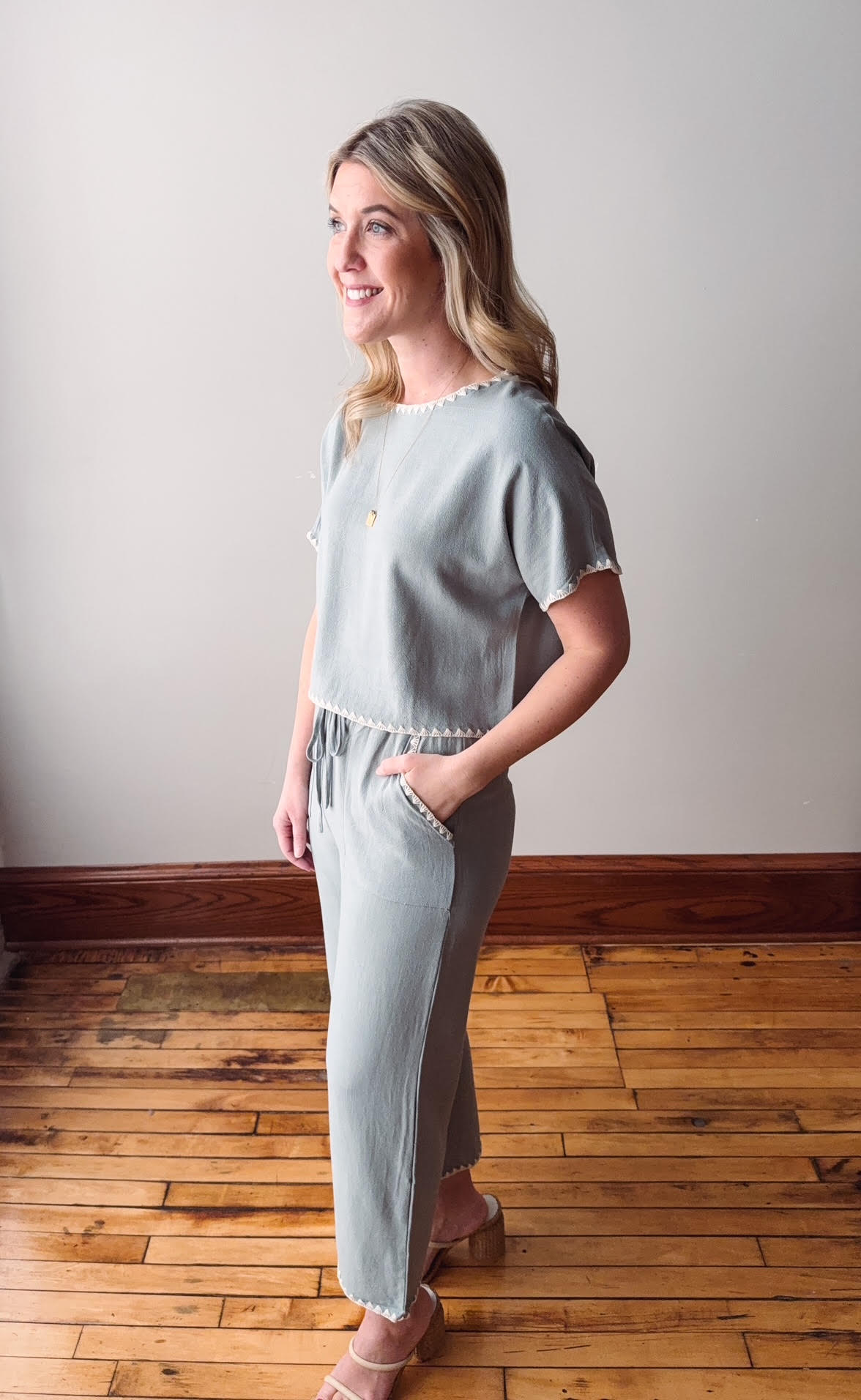 Woman wearing a light blue outfit standing on a wooden floor with a white wall background