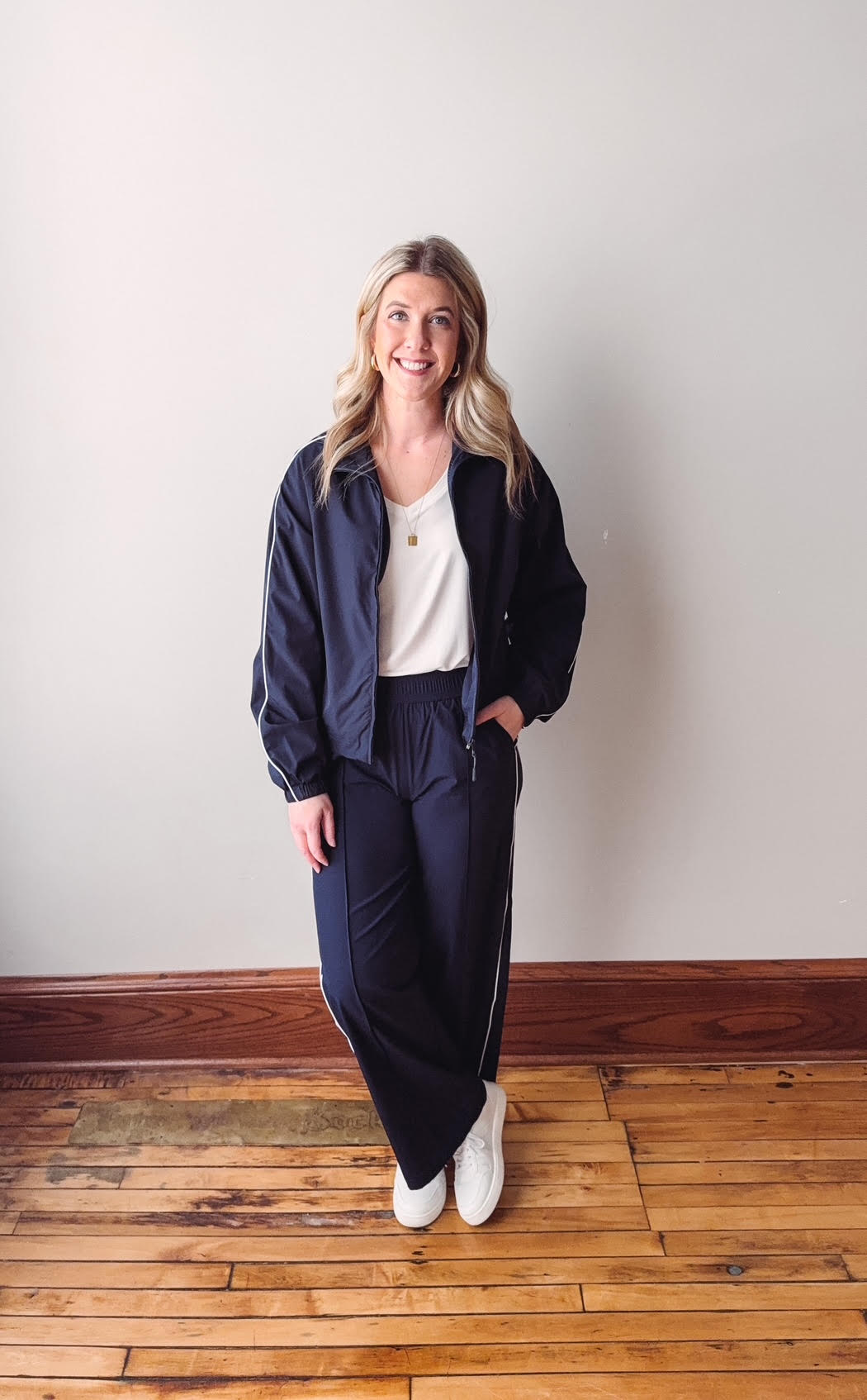Woman wearing a navy blue outfit standing on a wooden floor with a white wall background