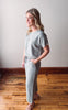 Woman wearing a light blue outfit standing on a wooden floor with a white wall background