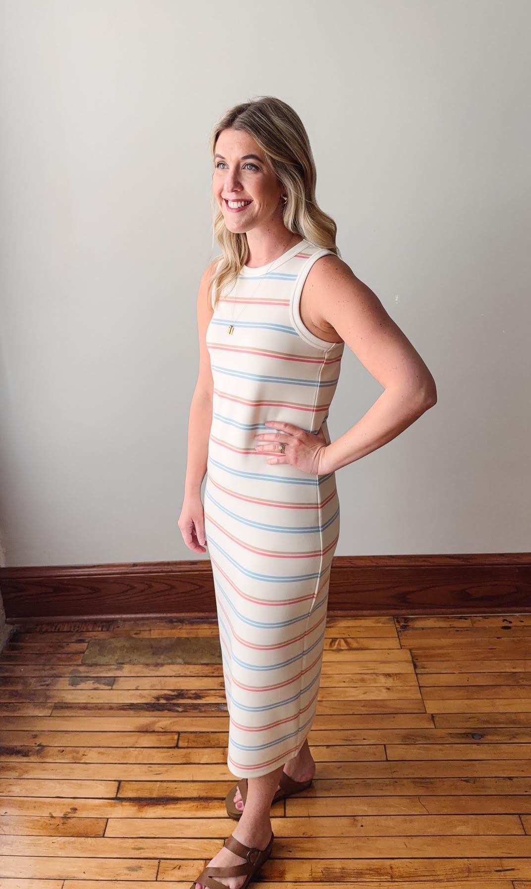 Woman wearing a striped dress standing on a wooden floor with a plain wall background