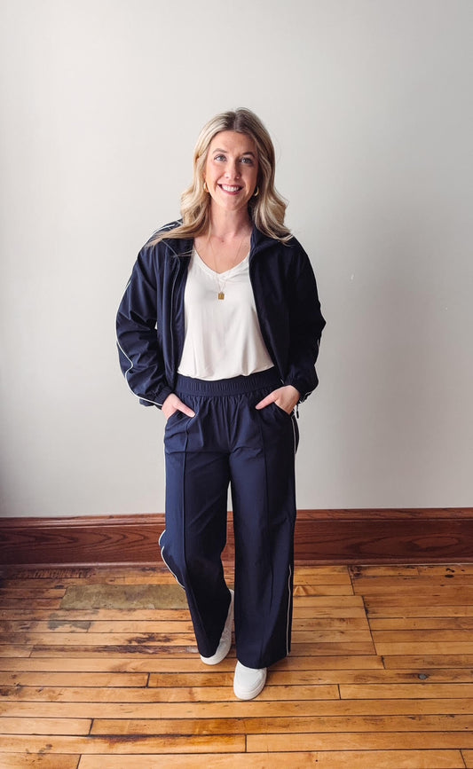 Woman wearing a navy tracksuit standing on a wooden floor with a white wall background