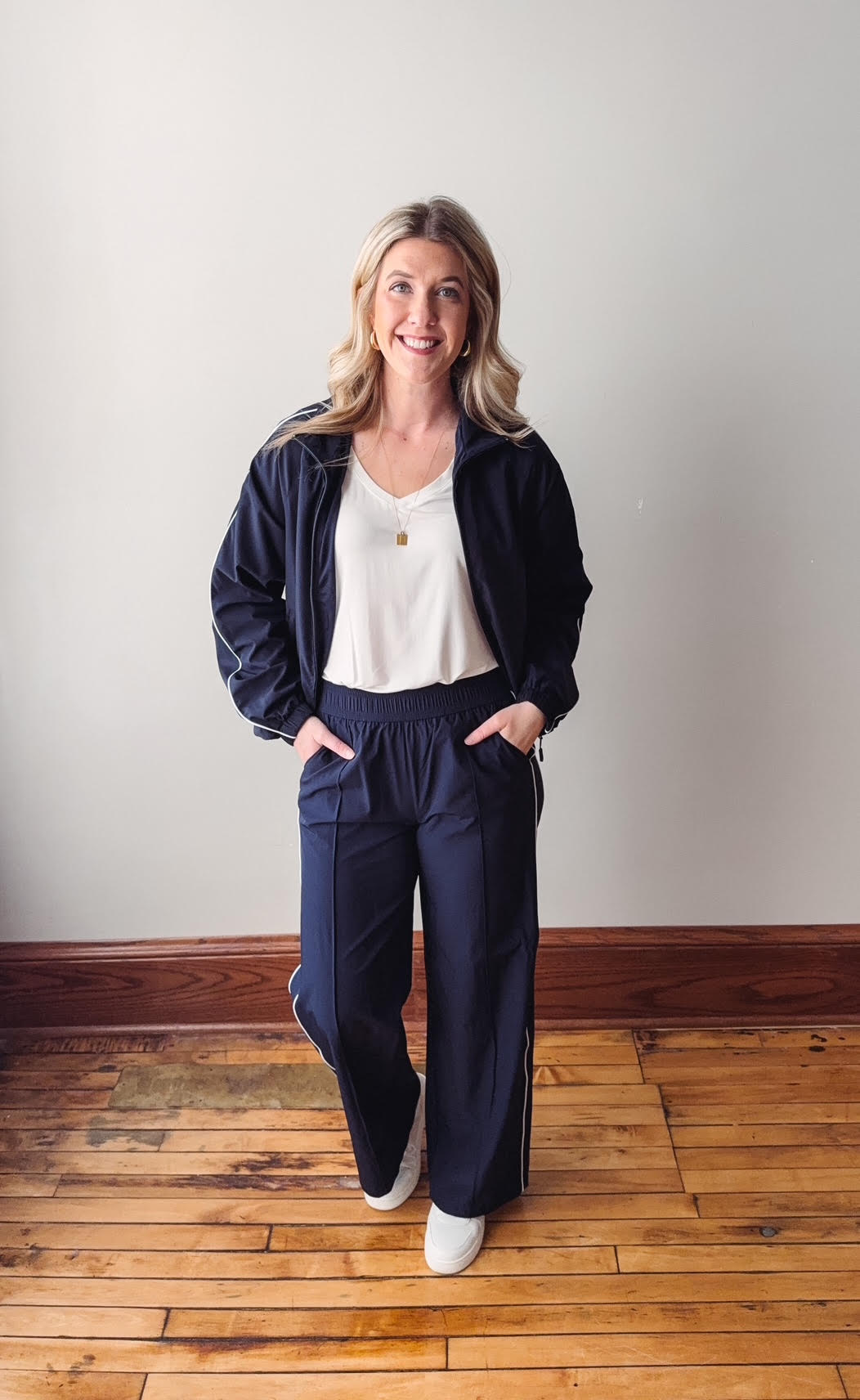 Woman wearing a navy tracksuit standing on a wooden floor with a white wall background