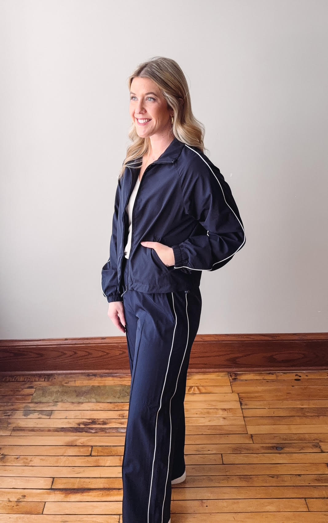 Woman wearing a navy tracksuit with white piping on a wooden floor.