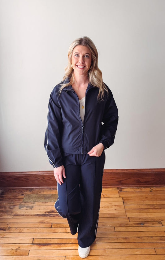 Woman wearing a navy tracksuit standing on a wooden floor with a white wall background