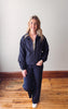 Woman wearing a navy tracksuit standing on a wooden floor with a white wall background