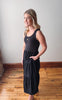 Woman wearing a black dress standing in a room with wooden flooring and a white wall.