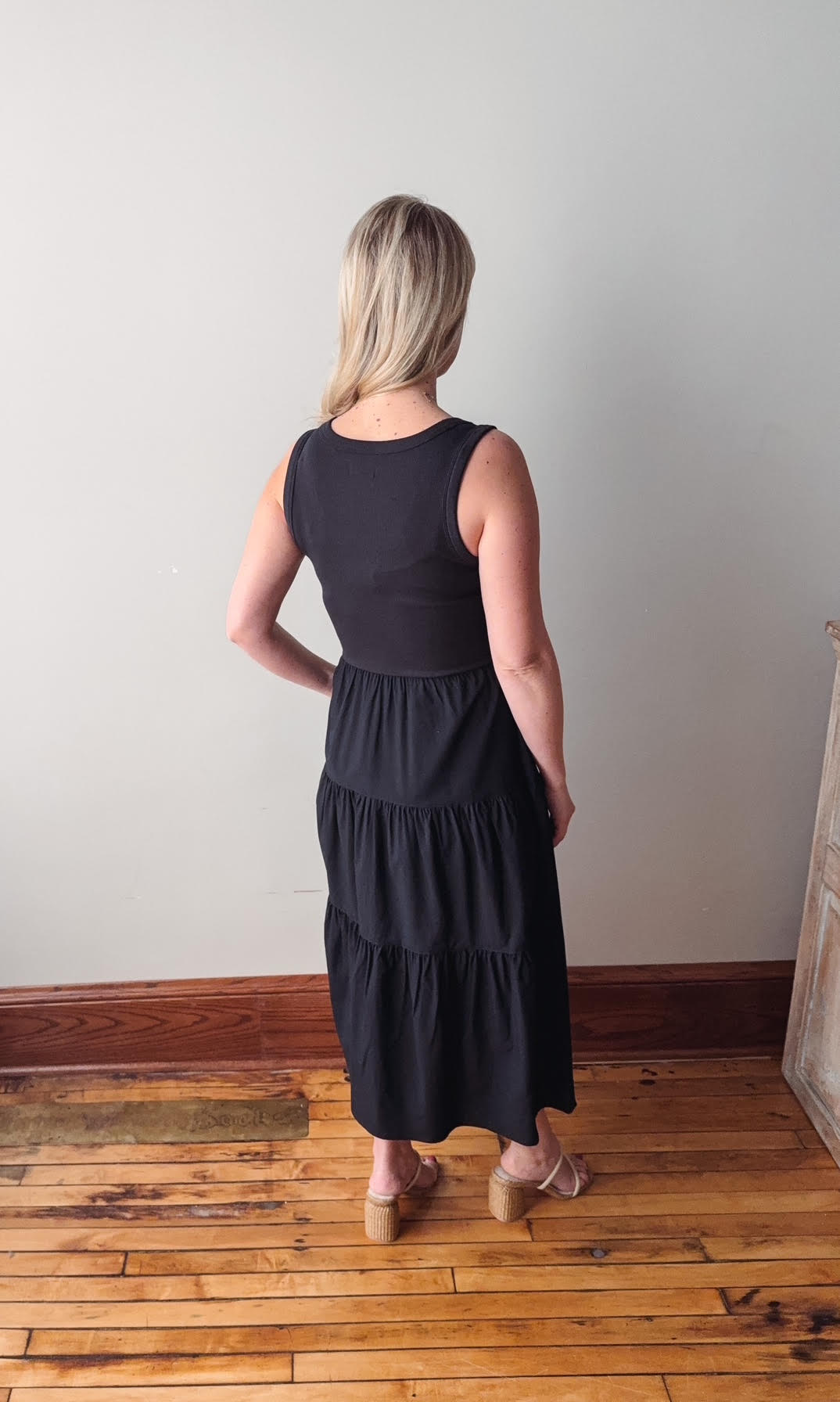 Woman wearing a black dress standing on a wooden floor with a white wall background