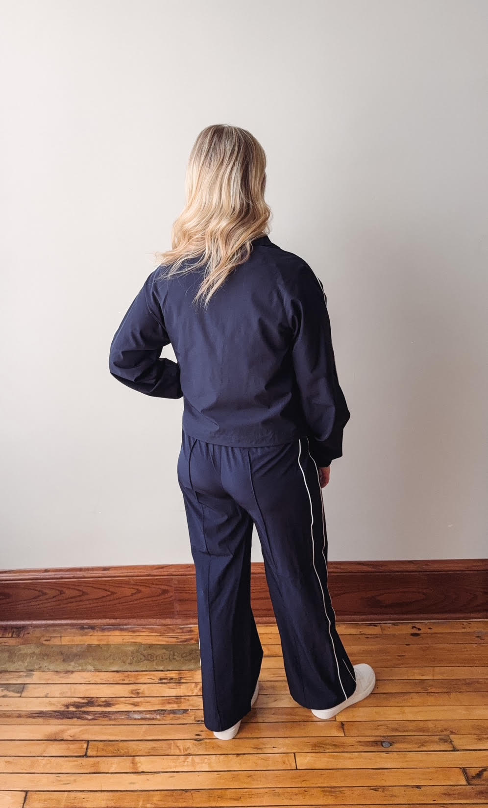 Person wearing a navy tracksuit standing on a wooden floor with a white wall background