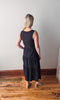 Woman wearing a black dress standing on a wooden floor with a white wall background