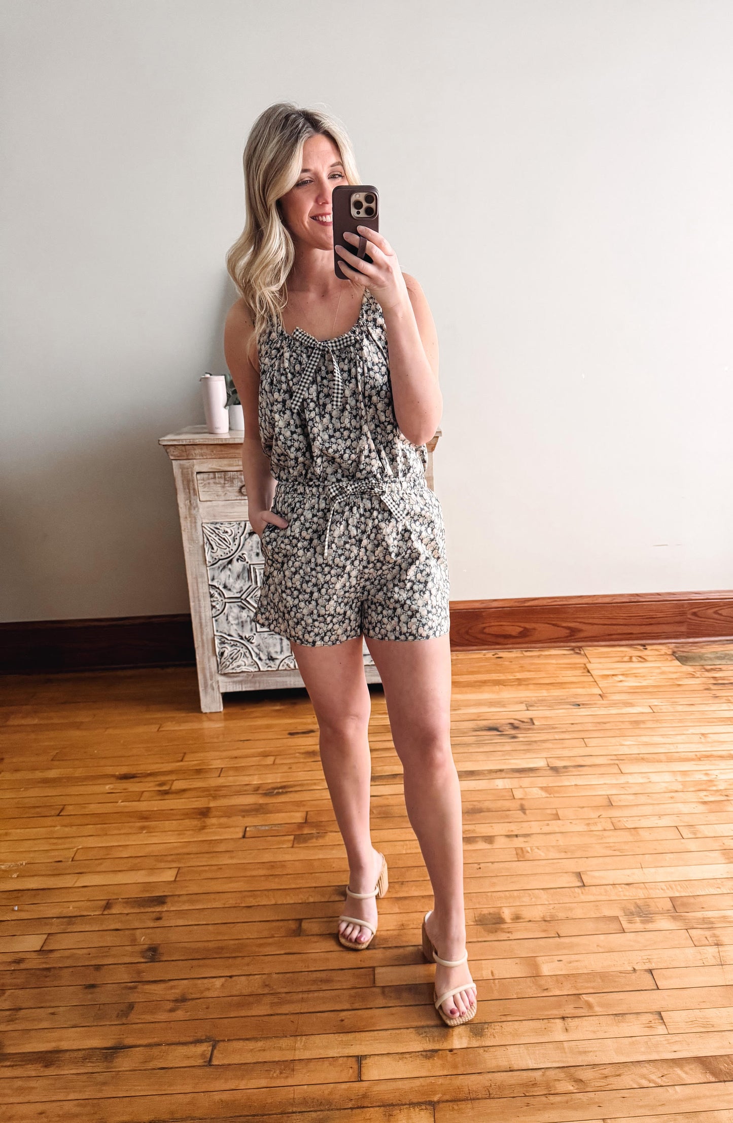 Woman taking a mirror selfie wearing a floral romper in a room with wooden flooring.