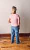 Person wearing a striped shirt and jeans standing on a wooden floor against a plain wall.