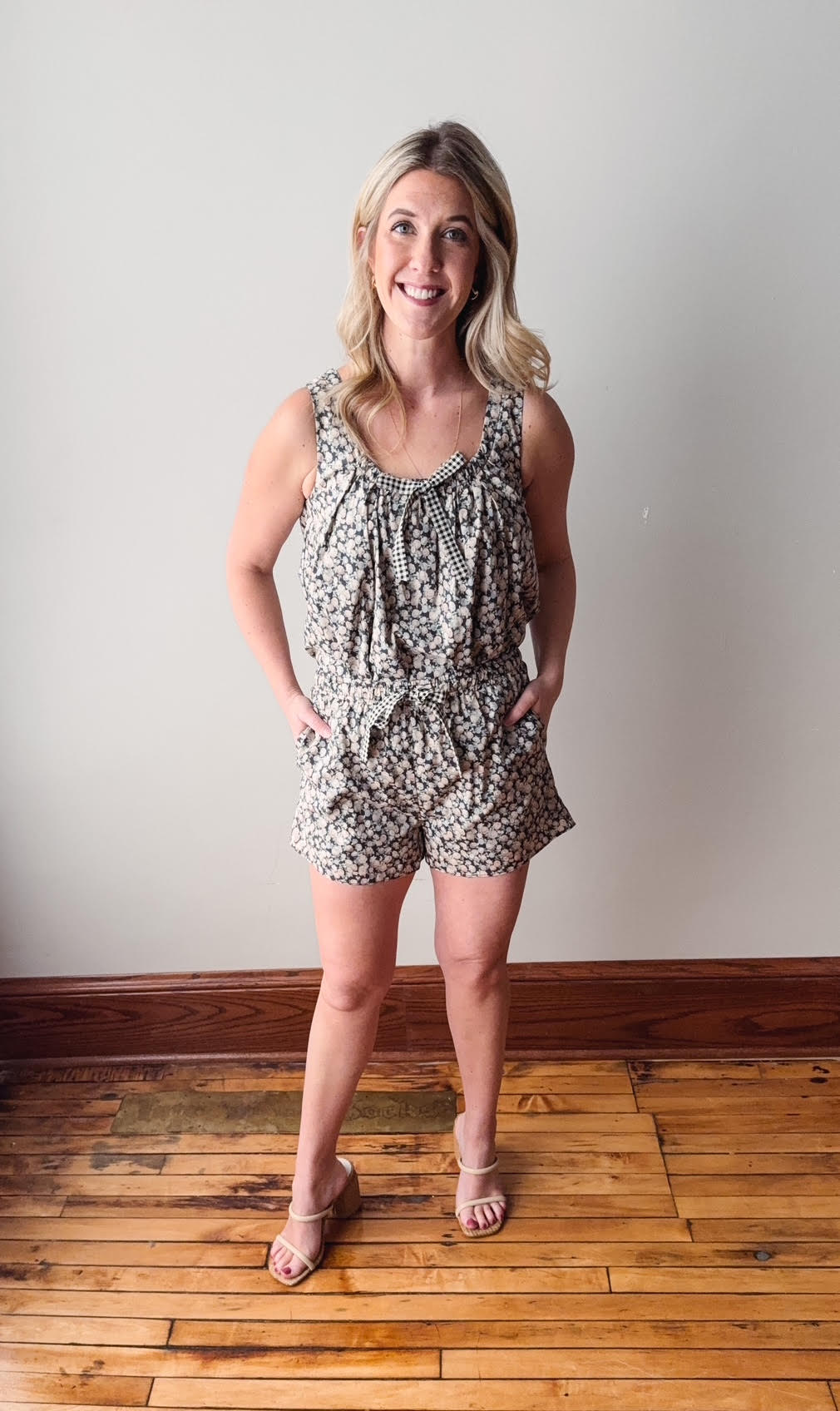 Woman wearing a patterned romper standing on a wooden floor with a plain wall background