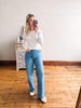 Woman taking a mirror selfie wearing a striped sweater and blue jeans in a room with wooden flooring.