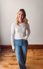 Woman wearing a striped sweater and jeans standing on a wooden floor.