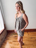 Woman in a patterned dress standing in a room with wooden flooring and a white wall.