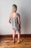 Woman wearing a floral romper standing on a wooden floor with a white wall background