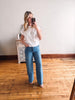 Woman taking a mirror selfie wearing a white shirt and blue jeans in a room with wooden flooring.