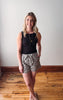Woman wearing a black sleeveless top and patterned shorts standing on a wooden floor.