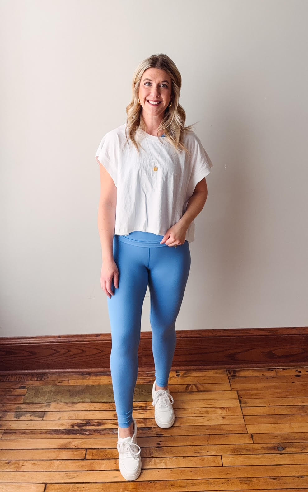 Woman wearing a white t-shirt and blue leggings standing on a wooden floor.