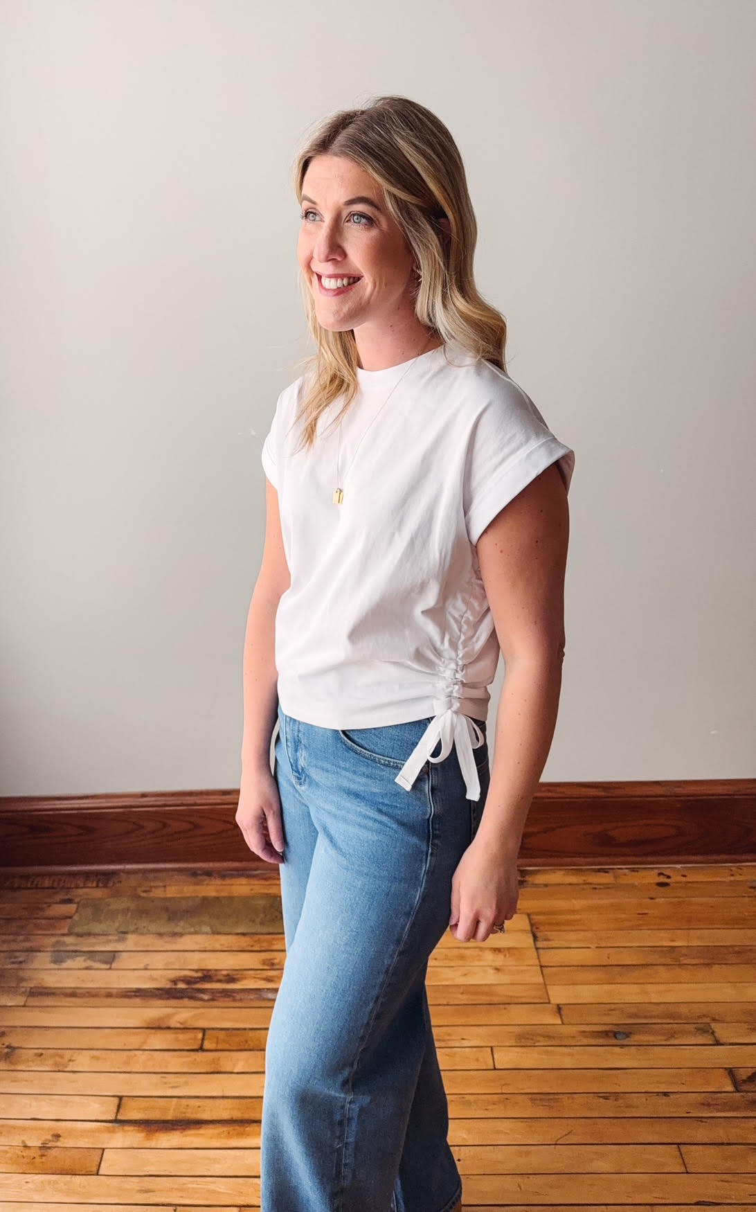 Woman wearing a white t-shirt and blue jeans standing in a room with wooden flooring.