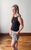 Woman wearing a black sleeveless top and patterned shorts standing on a wooden floor.
