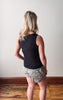 Person wearing a black sleeveless top and patterned shorts standing against a plain wall.