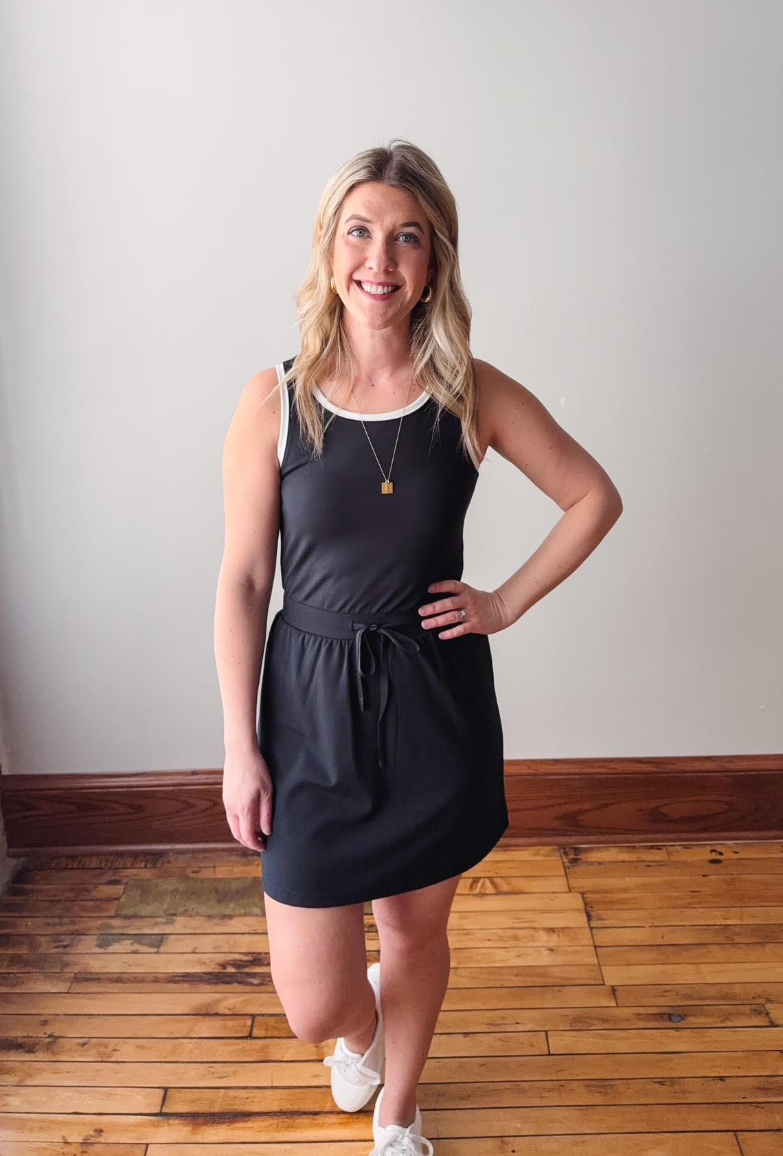 Woman wearing a black dress standing on a wooden floor with a plain wall background