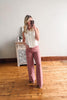 Woman taking a mirror selfie wearing a white blouse and pink pants in a room with wooden flooring.