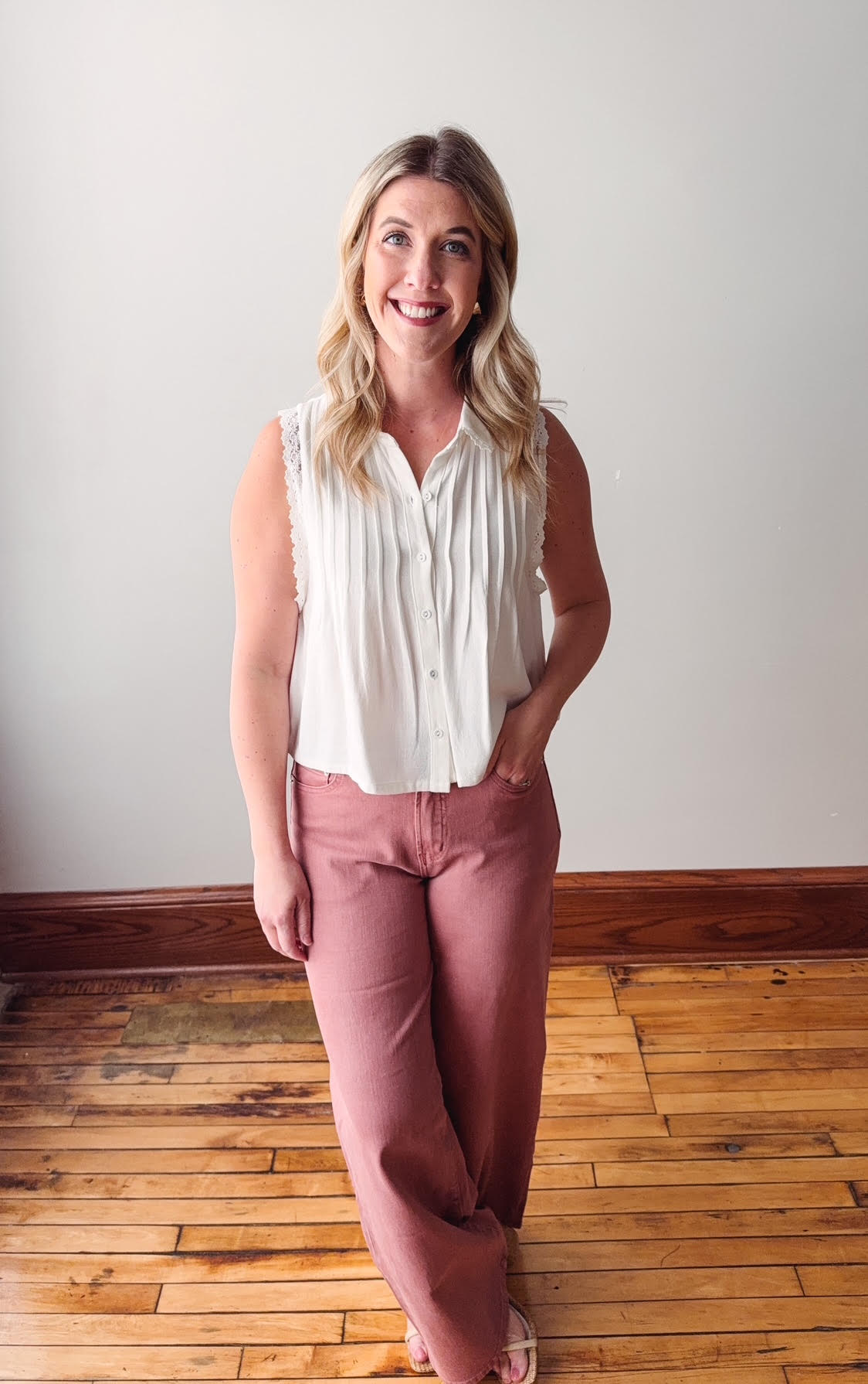 Woman wearing a white blouse and pink pants standing on a wooden floor.