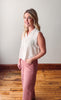 Woman wearing a white sleeveless top and pink pants standing on a wooden floor.