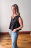 Woman wearing a black sleeveless top and light blue jeans standing in a room with wooden flooring.