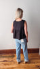 Person wearing a black sleeveless top and light blue jeans standing on a wooden floor with a white wall background.