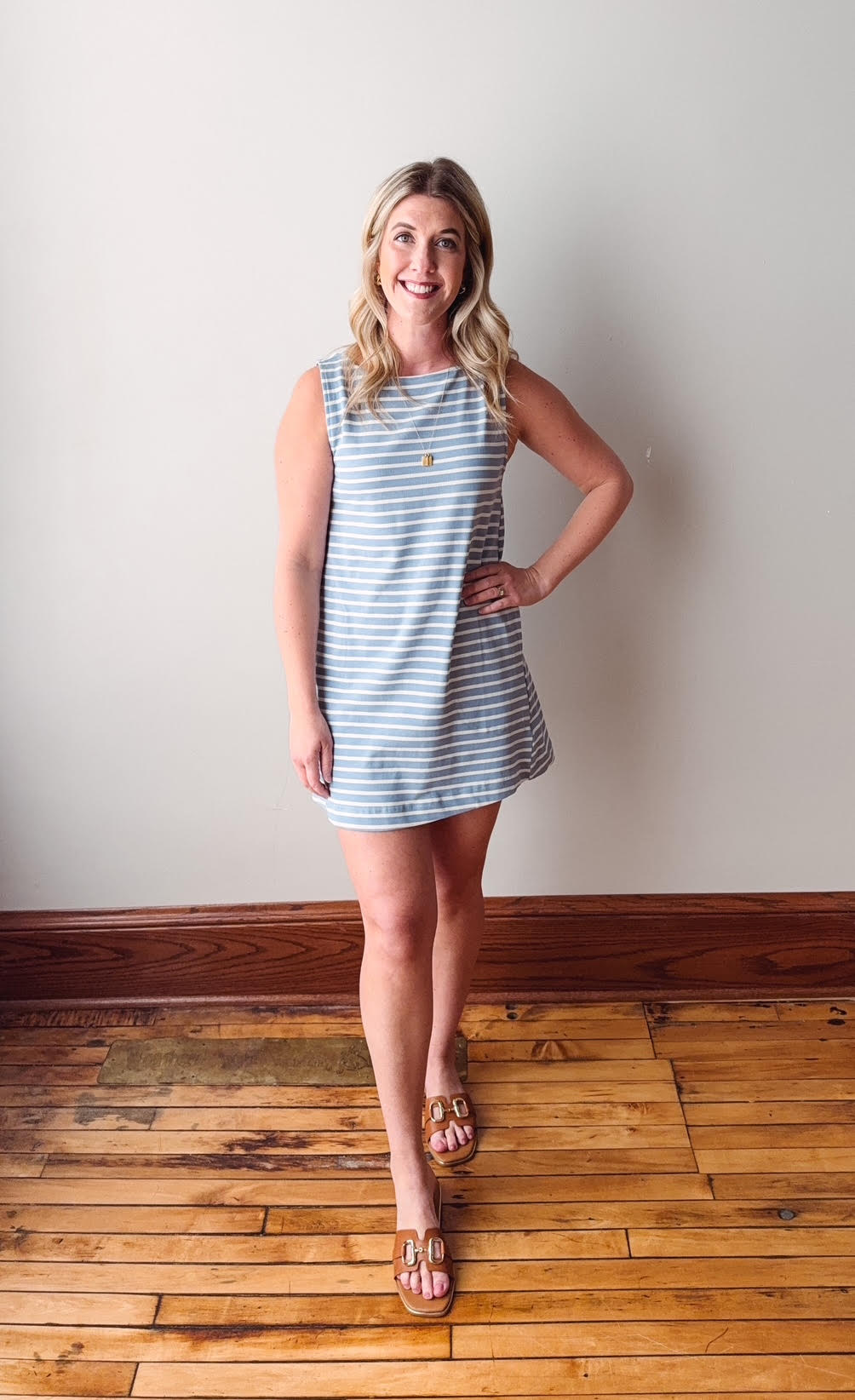 Woman wearing a striped dress standing on a wooden floor against a white wall